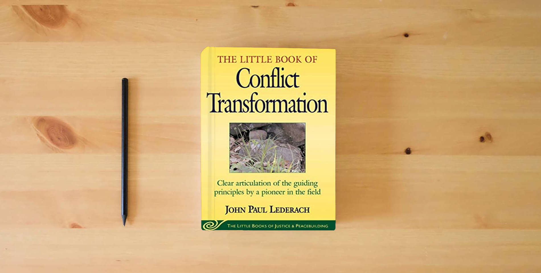The book Little Book of Conflict Transformation: Clear Articulation Of The Guiding Principles By A Pioneer In The Field (Justice and Peacebuilding) is on the table